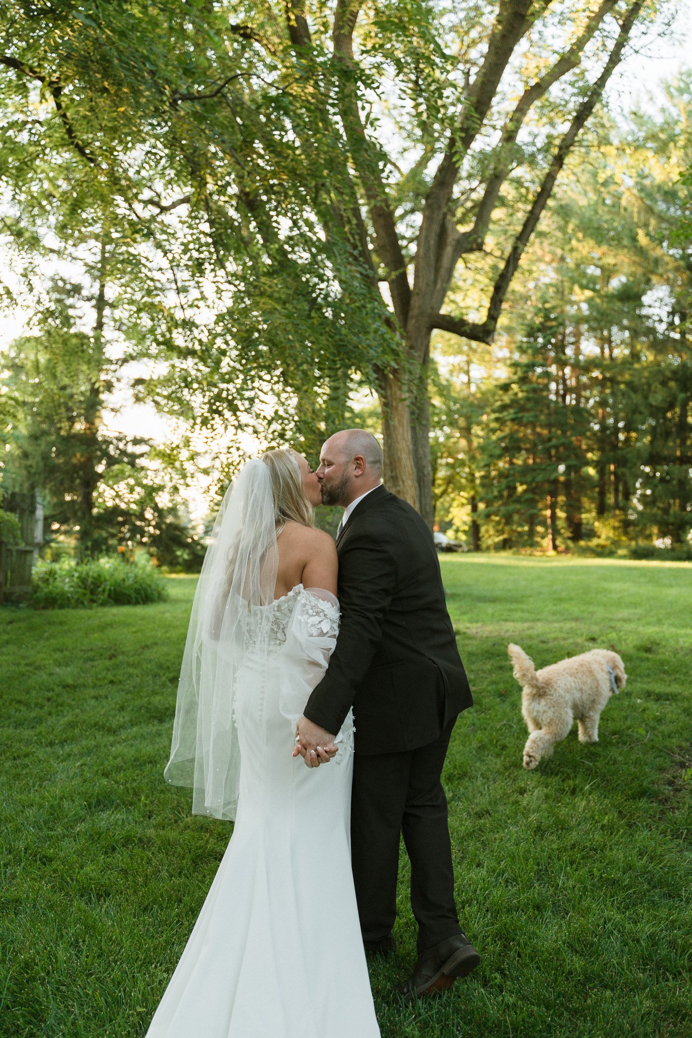 Couple kissing outdoors while their dog wanders nearby