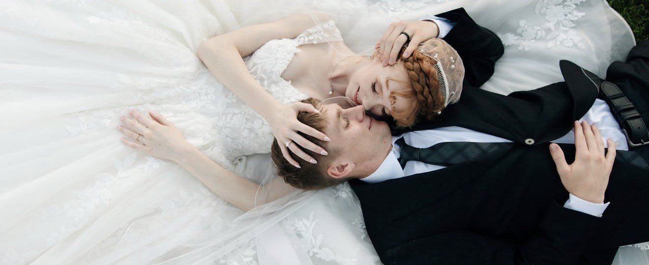 Couple photographed in the window openings of a ruined concrete wall with a floral installation